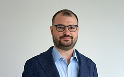 A man with bold hair and glasses smiling at the camera.