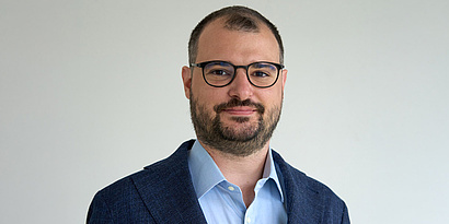 A man with bold hair and glasses smiling at the camera.