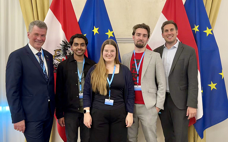 Four men and one woman, participants of the Hackathon, standing in front of the Austrian and European Flag.