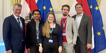 Four men and one woman, participants of the Hackathon, standing in front of the Austrian and European Flag.