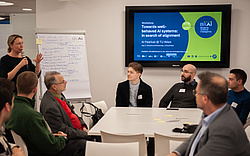 A workshop situation with researcher Marta Sabou standing in front and speaking and a group of participants listening and watching her.