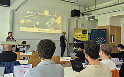 Robert Peharz standing in front of the audience, referring to the StartUp INspirAItion Day, giving a keynote.